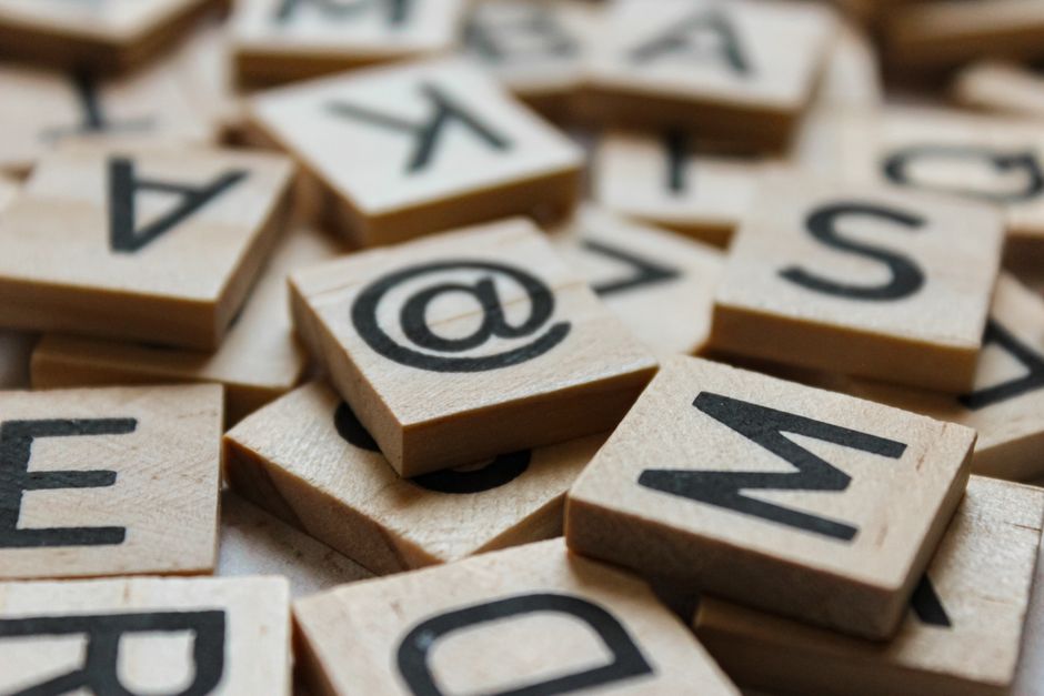Wooden letter tiles in a jumble with the @ symbol tile on top