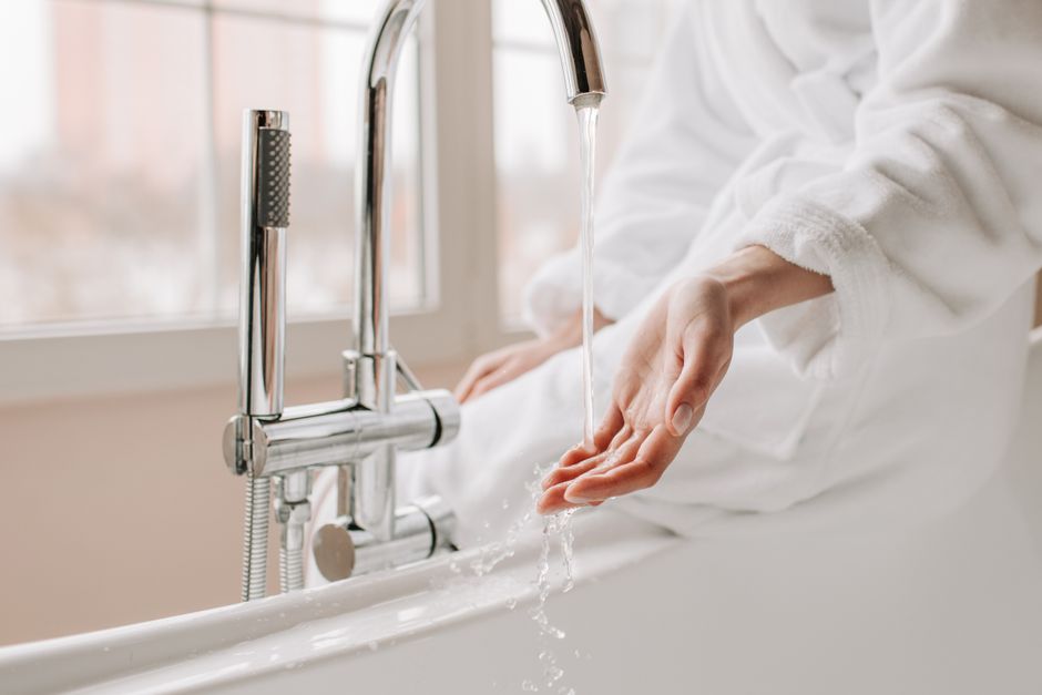 Hand held under a running bathtub faucet, fingers in the water