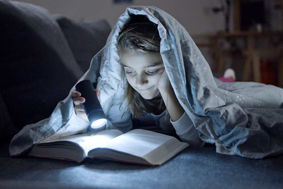 Curious kid reading a book by flashlight