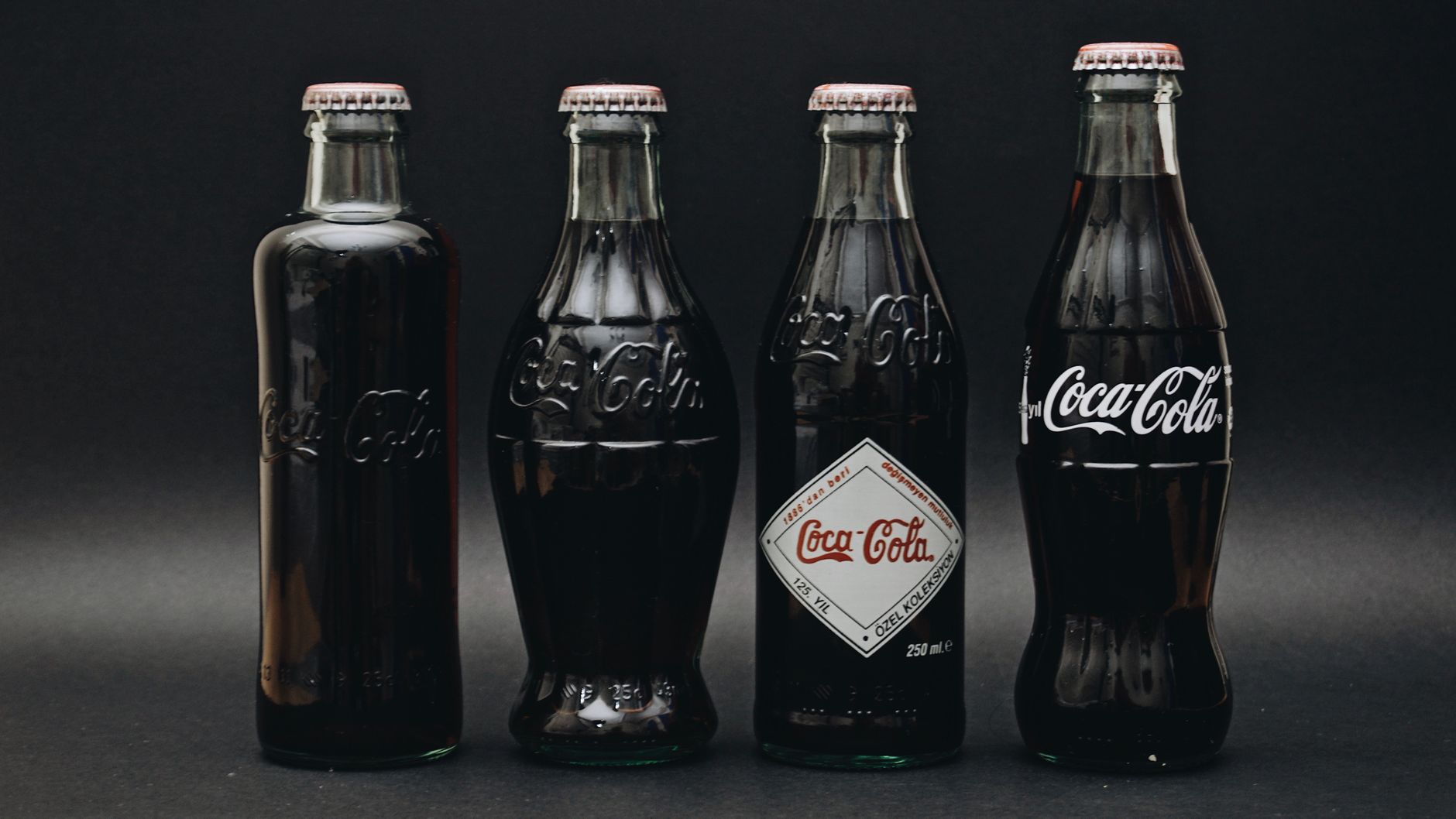 Four classic contour-shaped Coca-Cola glass bottles on a dark background