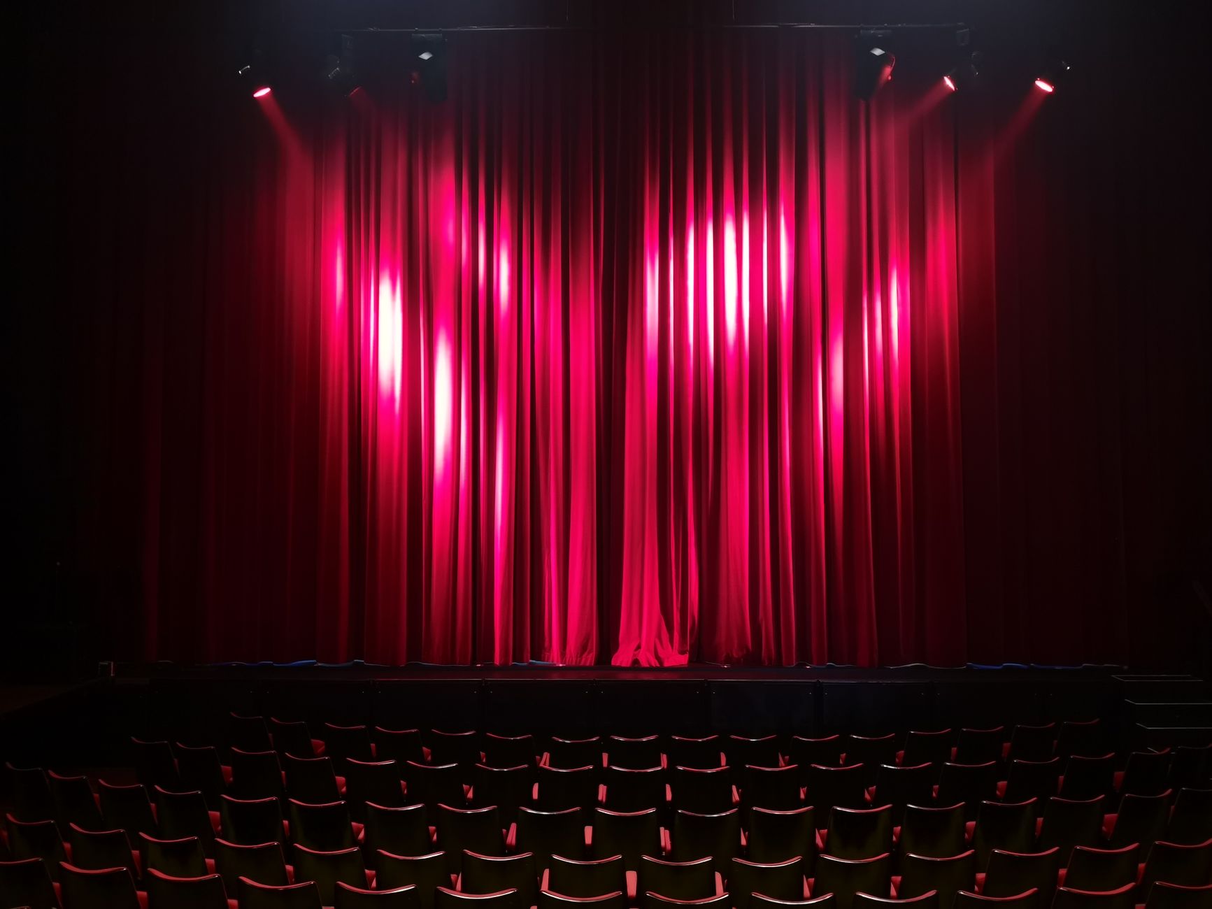An empty theatre stage with red curtains and rows of seats before a performance